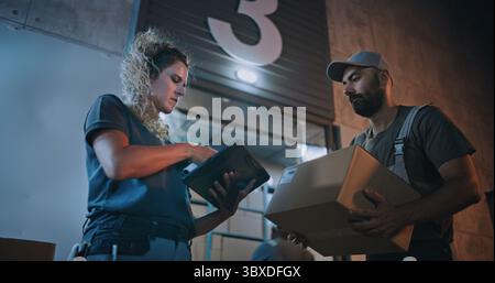 Travailleurs multiethniques transportant des boîtes en carton avec des commandes en ligne, des marchandises de Logistics Retail Warehouse la nuit. Gestionnaire d'inventaire féminin numérisation de colis avec scanner de code-barres, en utilisant un ordinateur tablette. Banque D'Images