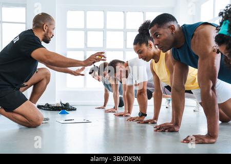 Groupe multiethnique de personnes sportives faisant de l'entraînement fonctionnel dans la salle de gym de classe d'entraînement divers athlètes effectuant des exercices de planche sous la direction de Banque D'Images