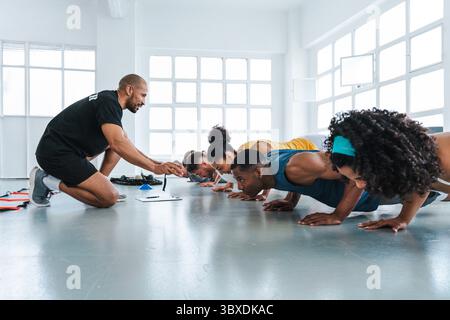 Groupe multiethnique de personnes sportives faisant de l'entraînement fonctionnel dans la salle de gym de classe d'entraînement groupe diversifié d'athlètes effectuant des pompes synchronisées sous p Banque D'Images