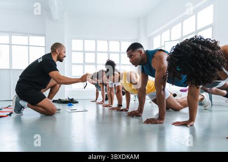 Groupe multiethnique de personnes sportives faisant de l'entraînement fonctionnel dans le gymnase de classe d'entraînement divers athlètes effectuant des pompes synchronisées pendant la fonctiona Banque D'Images