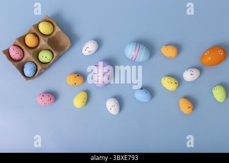 De beaux œufs multicolores décoratifs sont dispersés sur un fond bleu clair, vue de dessus Banque D'Images