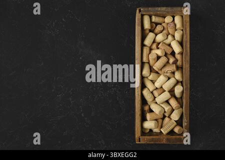 Une boîte en bois remplie de bouchons de vin assortis repose sur une surface sombre. Les bouchons varient en taille et en forme, présentant une collection de différents vins bo Banque D'Images
