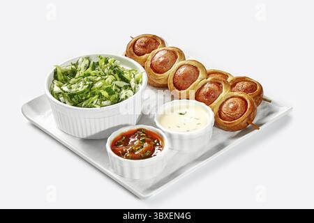 Plateau de cochons fraîchement cuits dans une couverture, salade verte d'accompagnement, et trempettes assorties servies pour le petit déjeuner sur fond blanc Banque D'Images