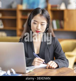 Femme asiatique étudiant cours en ligne, enseignement à distance sur ordinateur portable. Femme d'affaires japonaise travaillant. Travail indépendant écrit dans le bloc-notes Banque D'Images