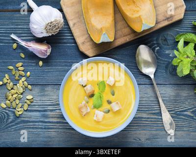 Soupe crémeuse de citrouille avec croûtons et graines sur fond de bois bleu foncé, ail, menthe, tranches de citrouille. Vue de dessus Banque D'Images