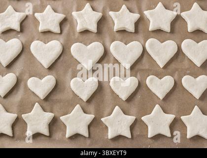 Nourriture, biscuits crus sous forme d'étoiles et de coeurs sur une plaque à pâtisserie avec parchemin, vue de dessus. Étape de cuisson de délicieux gâteaux faits maison Banque D'Images