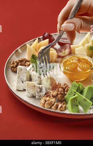 Femme perçant un morceau de fromage bleu à la fourchette, savourant un délicieux plateau de fromage servi traditionnellement avec des noix, du miel et des raisins, présenté sur l'élég Banque D'Images