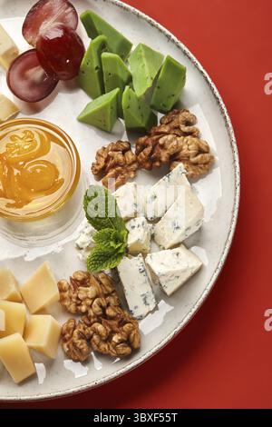 Assiette de fromage délicieuse avec différents types de fromage, noix, raisins, miel et menthe, créer une expérience culinaire savoureuse et visuellement attrayante Banque D'Images