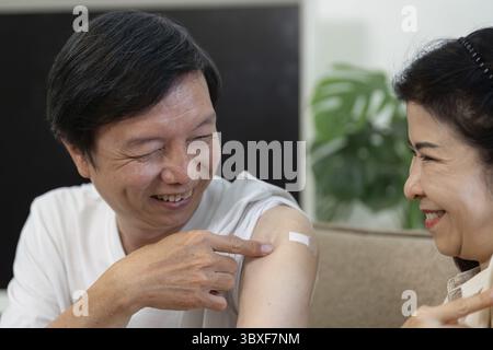 Un couple de personnes âgées partage un moment joyeux, montrant leurs bandages vaccinaux, mettant en valeur le soutien et la compagnie Banque D'Images