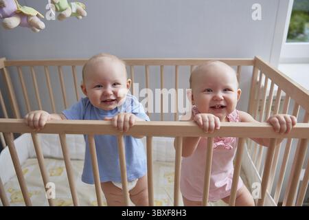 Les enfants jumeaux, garçon et fille, sourient en se tenant debout le berceau Banque D'Images