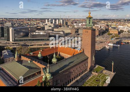 Vue aérienne de la brique rouge de l'hôtel de ville de Stockholm contrastant avec les eaux bleues, face à l'horizon urbain, Stockholm, Comté de Stockholm, Suède. Banque D'Images
