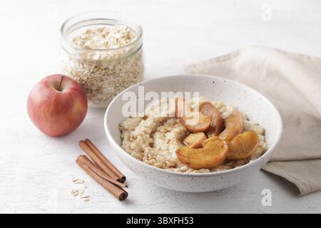 Nourriture, bouillie d'avoine sucrée avec des tranches de pomme cuites au four, cannelle et sauce caramel dans un bol gris sur un fond clair avec des ingrédients. Maison délicieuse Banque D'Images
