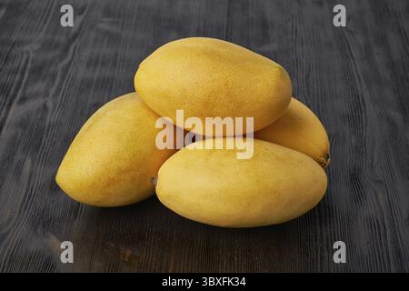 Quatre mangues entières de fruits sur table en bois. Gros fruits jaunes mûrs et juteux sur fond sombre Banque D'Images