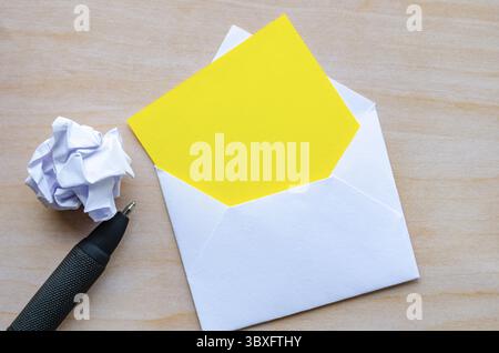 Vue de dessus du bloc-notes jaune vide à l'intérieur d'une enveloppe avec du papier froissé et un stylo avec un espace personnalisable pour le texte Banque D'Images