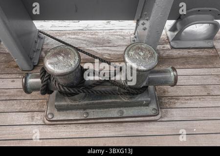 Une borne métallique double avec cordage noir sur un pont en bois, une partie d'un navire, borne de bateau d'un vieux navire Banque D'Images