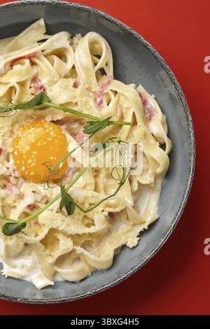 De délicieuses pâtes carbonara sont garnies de pousses de pois frais et servies dans un bol moderne Banque D'Images