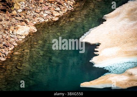 Un paysage serein avec un plan d'eau bleu clair bordé par un terrain rocheux et des plaques de glace. Le contraste entre l'eau et la glace crée Banque D'Images