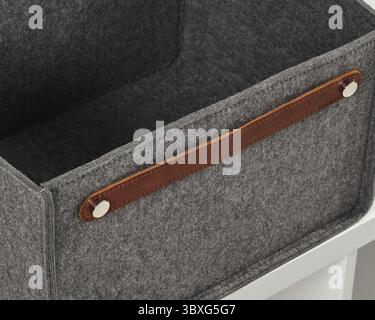 Gros plan d'une boîte de rangement vide en feutre gris avec une poignée en cuir marron, parfaite pour organiser n'importe quel espace Banque D'Images