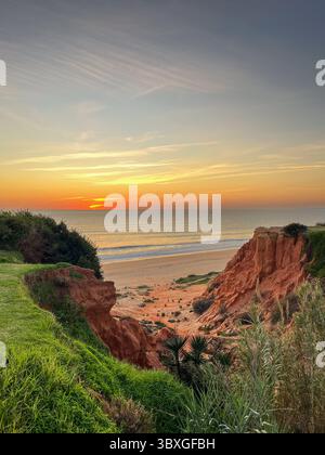 Paysage côtier au coucher du soleil, présentant des couleurs vibrantes dans le ciel, plage de sable et falaises rouges frappantes, évoquant un sentiment de tranquillité et d'être naturel Banque D'Images