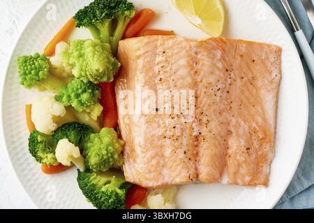 Macro saumon vapeur et légumes, Paleo, céto, fodmap, régime DASH. Régime méditerranéen avec poisson vapeur. Concept sain, plaque blanche sur table grise, g Banque D'Images