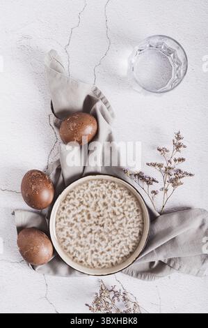 Nourriture, oeufs de Pâques naturellement colorés, assiette, couverts et verre d'eau sur le dessus de la table et vue verticale Banque D'Images