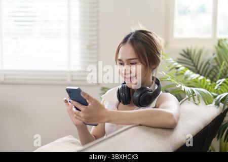 Une jeune femme profite d'un après-midi de détente à la maison en écoutant de la musique avec des écouteurs tout en utilisant son smartphone Banque D'Images