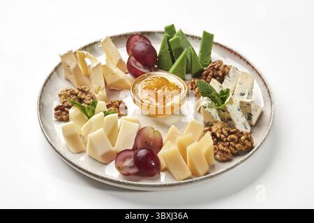Sélection de fromages assortis traditionnellement servis avec des noix, des raisins et un bol de miel sur une assiette en céramique, sur fond blanc. Délicieux hors-d'œuvre Banque D'Images