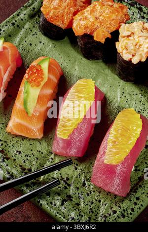 Des sushis fraîchement préparés avec du saumon, du thon et diverses garnitures, servis sur une assiette verte avec des baguettes, mettant en valeur l'art culinaire japonais vibrant Banque D'Images