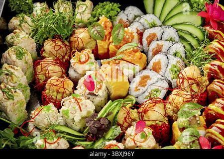 Assiette de sushis vibrante avec un assortiment de maki, uramaki et nigiri, garnie de légumes frais et de fleurs comestibles Banque D'Images