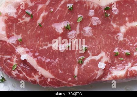 Gros morceau entier de viande de bœuf crue, striploine. Steak avec assaisonnement, huile et sel. Vue de dessus, gros plan, macro Banque D'Images