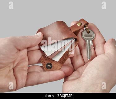 Mains masculines présentant porte-clés en cuir marron fabriqué à la main gravé avec PAPA avec des photos de famille imprimées sur fond gris. Concept de réfléchi Banque D'Images