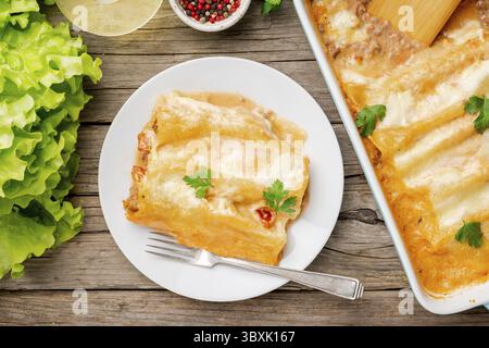 Cannelloni avec remplissage de boeuf haché, tomates, cuit avec sauce tomate bechamel, vue sur le dessus, vieux fond en bois sombre Banque D'Images