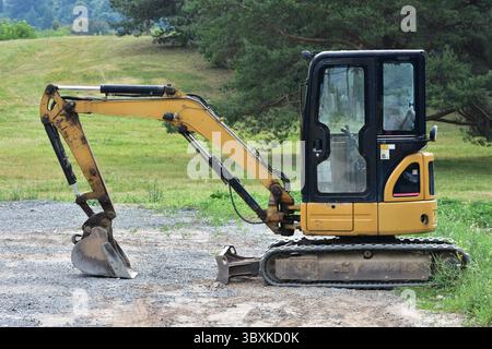 La pelle caterpillar compacte jaune repose sur du gravier près d'un champ herbeux. Équipement de construction utilisé pour le creusement, les travaux de terrassement et les petits projets. Banque D'Images