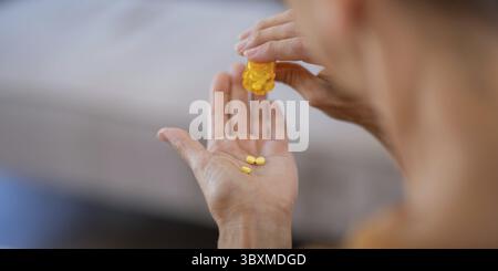 Une femme âgée versant des pilules d'une bouteille pour ses médicaments quotidiens, mettant l'accent sur la gestion de la santé à la maison Banque D'Images
