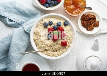 Gruau porridge avec bleuets, framboises, confiture et noix dans un bol blanc, diète au tableau de bord avec baies, fond blanc, vue de dessus. Un petit déjeuner sain Banque D'Images