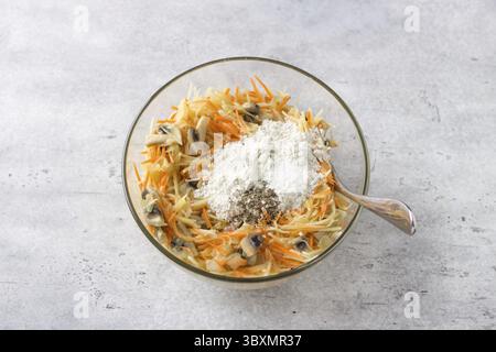 Nourriture, bol en verre avec un mélange de pommes de terre râpées, carottes, œufs, champignons frits avec oignons et farine avec épices pour faire une délicieuse tarte aux pommes de terre Banque D'Images