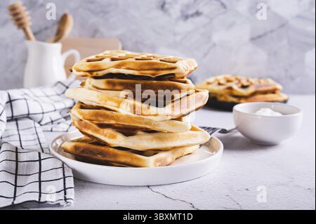 Nourriture, pile de gaufres belges fraîchement cuites sur l'assiette et crème sure dans un bol sur la table Banque D'Images