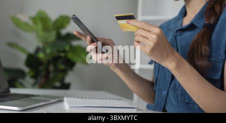 Une femme vérifie ses coordonnées financières sur son smartphone tout en tenant une carte de crédit, mettant en valeur l’approche moderne de la gestion financière et de l’épargne Banque D'Images