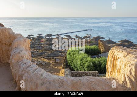 Vue panoramique sur la plage de Ras Umm El Sid. Beau lever de soleil sur la mer Rouge avec des rivages rocheux, plage de sable avec parasols et premiers rayons de soleil, Sharm El S. Banque D'Images