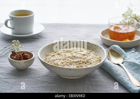 Flocons d'avoine entiers, grand bol de porridge avec beurre pour le petit déjeuner, repas du matin. Vue latérale, gros plan, table grise. Régime végétalien savoureux sain Banque D'Images