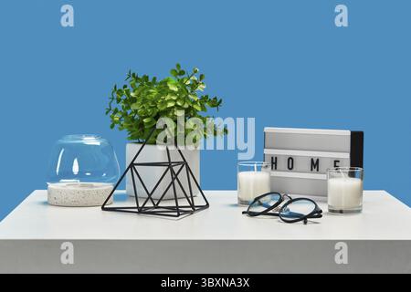 Table blanche avec bougies et chandelier en verre, plante verte en pot, verres à bords noirs, triangle en fer décoratif, élément de décoration. Bleu Banque D'Images