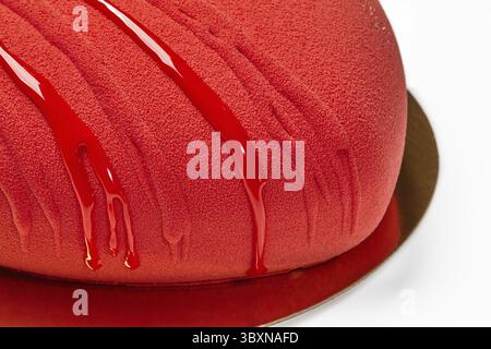Vue rapprochée d'un gâteau en mousse rouge en forme de cœur à la texture veloutée, arrosé de glaçage brillant sur une base dorée réfléchissante. Dessert design élégant Banque D'Images