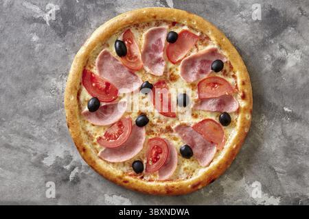 Pizza classique fine appétissante avec bord bruni croustillant surmonté de tranches de jambon, tomates fraîches et olives noires à base de fromage fondu, vue de dessus A. Banque D'Images