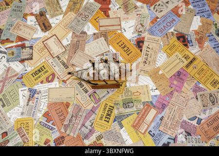 Sibiu, Roumanie - 05 novembre 2024. Modèle de bateau avec des voiles sur un tas de billets vintage du monde entier, théâtre, film, concerts, transport, ho Banque D'Images