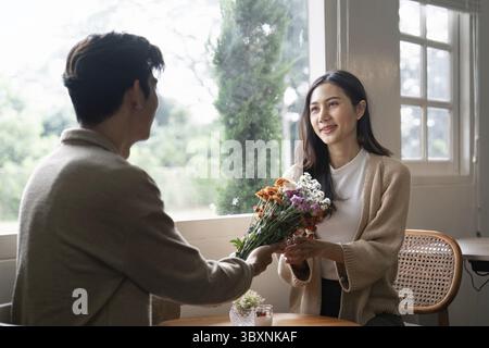 Un couple aime échanger un bouquet de fleurs près d’une fenêtre ensoleillée, soulignant un moment d’affection et de chaleur Banque D'Images