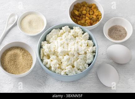 Nourriture, ingrédients pour casserole de fromage cottage : fromage cottage, cassonade, sucre vanillé, raisins secs, œufs, semoule, sel sur un fond gris clair, Banque D'Images