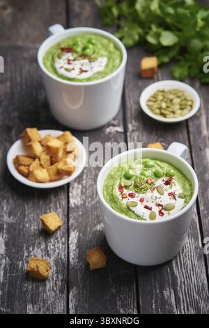 Soupe à la crème de brocoli, verticale. Purée de légumes verts dans deux grandes tasses blanches. Alimentation de la soupe végétalienne de brocoli, courgettes, pois verts sur fond de bois foncé Banque D'Images