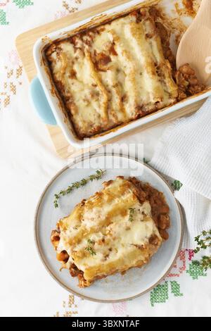Pâtes cannelloni avec garniture de bœuf haché, tomates, cuites à la sauce tomate au béchamel et à la mozzarella. Cuisine italienne classique, nappe blanche Banque D'Images