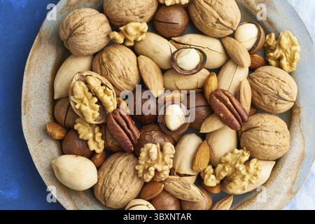Bleu classique dans la nourriture. Mélange de noix sur une assiette - noix, amandes, pacanes, macadamia et couteau pour ouvrir la coquille. Nourriture végétalienne saine. Manger propre, balan Banque D'Images