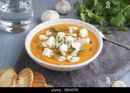 Purée de soupe à la crème Pupmkin avec ricotta, déjeuner végétarien diététique sur une table en bois bleu, vue de côté. Verre d'eau, pain grillé, persil, ail Banque D'Images